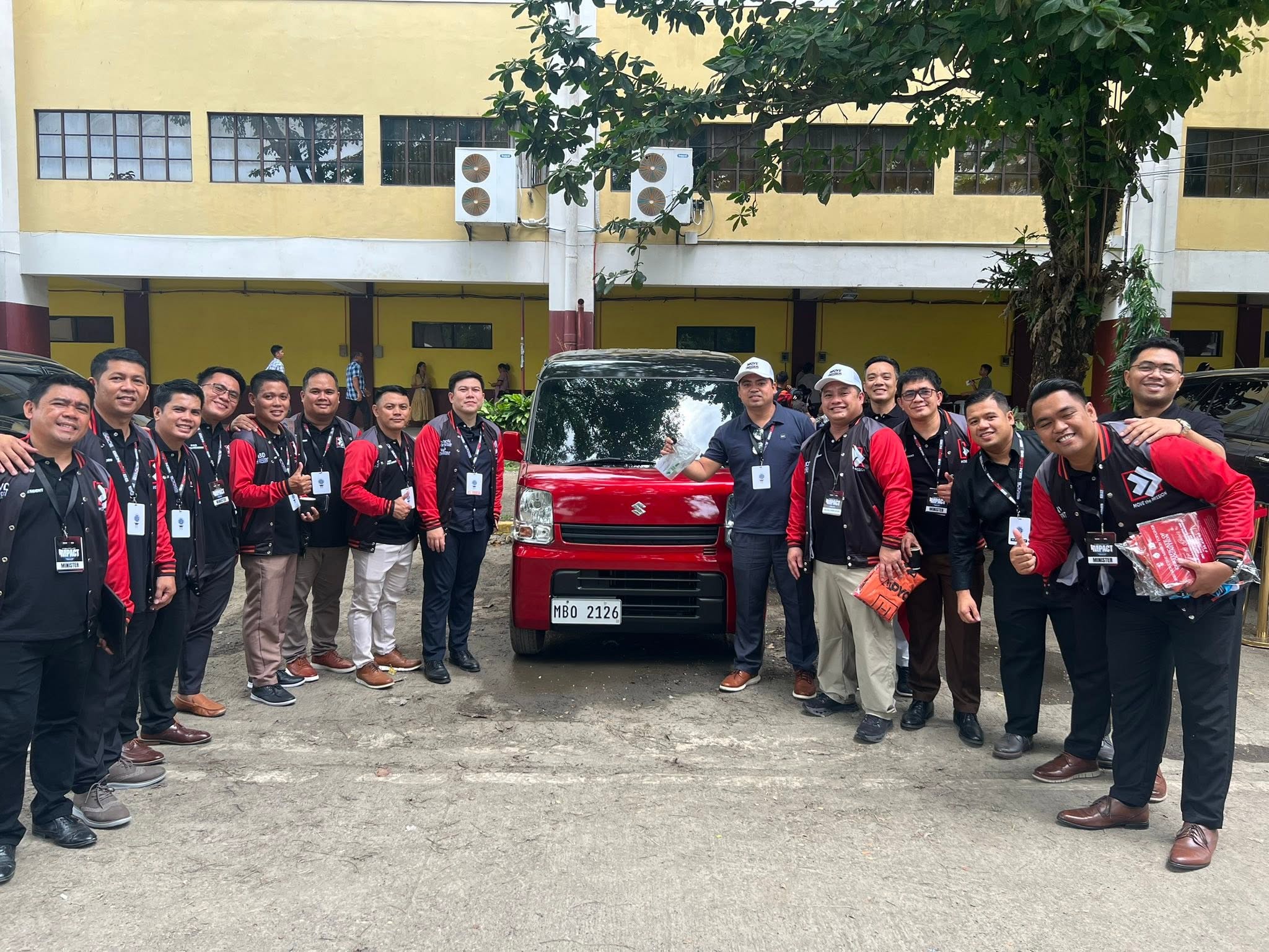 Ministry leaders in Move The Mission red and black jackets celebrating beside the Suzuki Multicab with Ptr. Joseph Carino at center