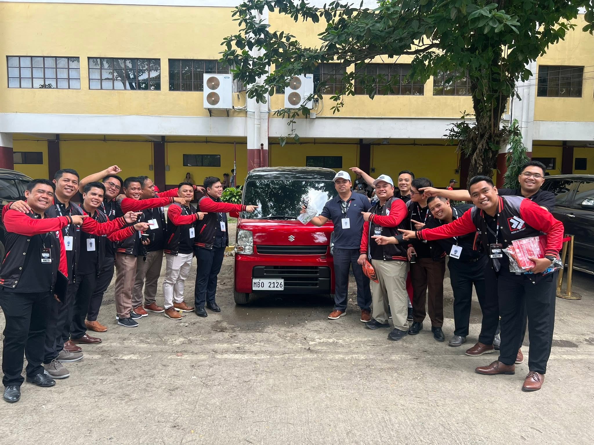 A large group of ministers all pointing toward Ptr. Joseph Carino and the red Suzuki Multicab in a playful celebratory pose