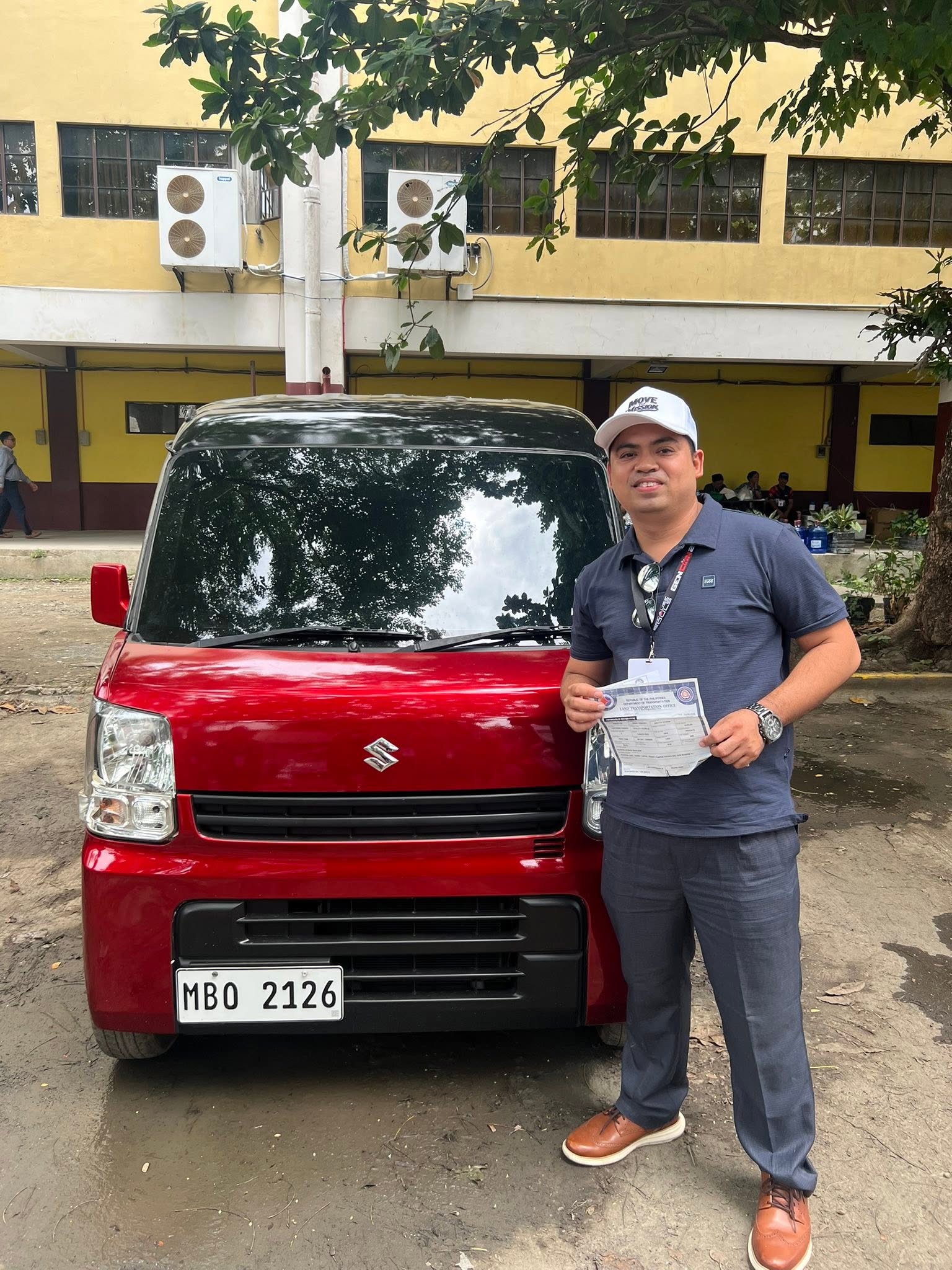 Ptr. Joseph Carino holding the official vehicle transfer papers beside the brand-new Suzuki Multicab, wearing a Move The Mission cap